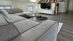 A modern loft apartment with a large sectional sofa, a flat-screen TV, and a dining area. - Fischerstuv Modern Retreat (Toenning)