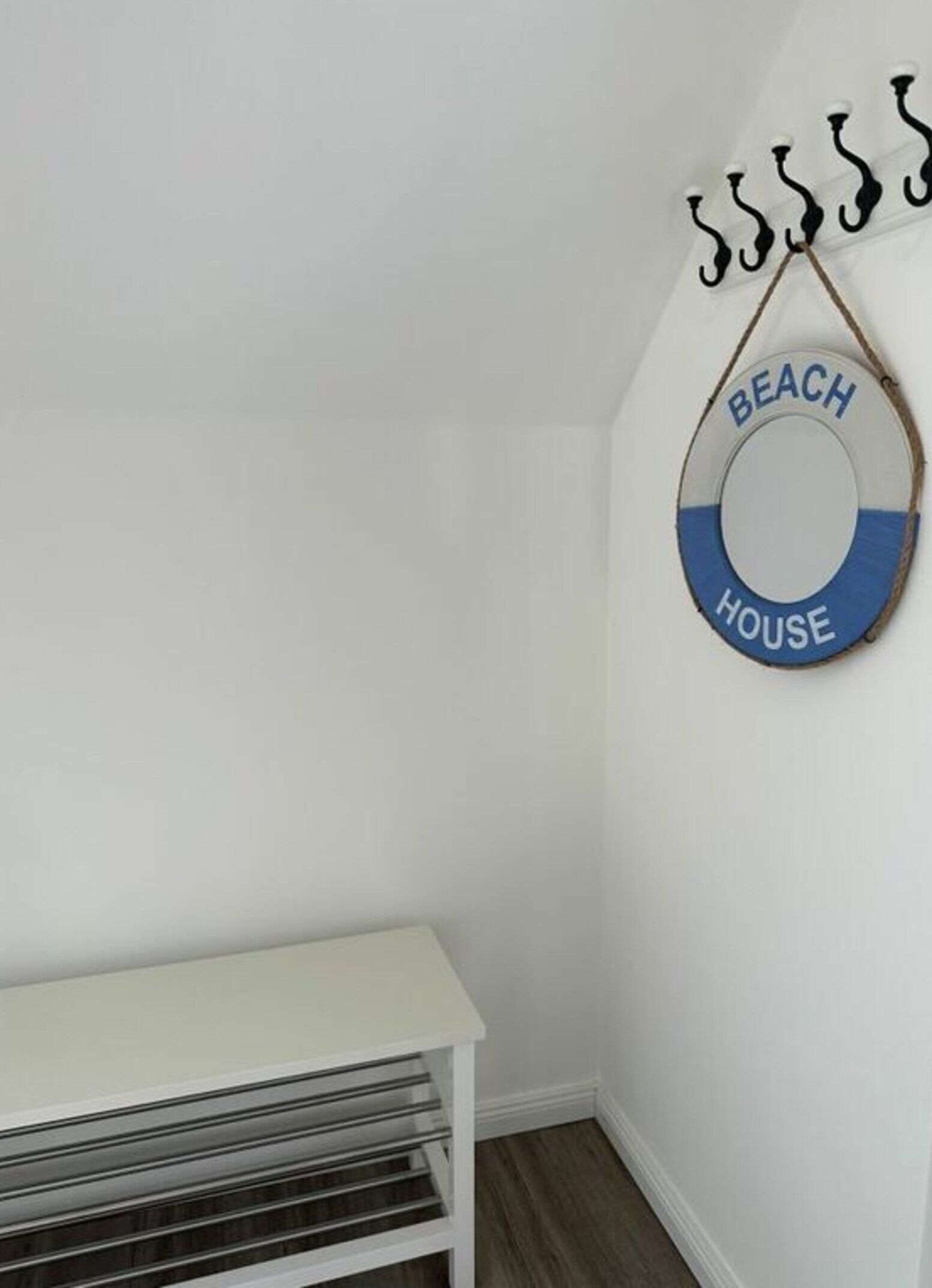 A white wall with a circular sign reading "BEACH HOUSE" and a white bench.
