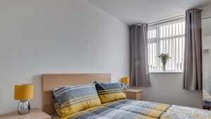 Une chambre à coucher avec un lit, deux lampes de chevet, une table de chevet, une fenêtre avec des rideaux et une vue sur l’extérieur.