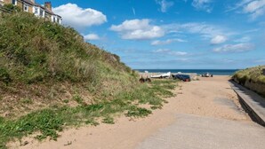 Une plage de sable avec un chemin pavé, une rangée de maisons et un ciel bleu dégagé.