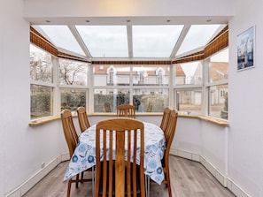 A dining area with a table and chairs, large windows, and a view of houses. - 6 Person Holiday Home in Albaek (Aalbaek)