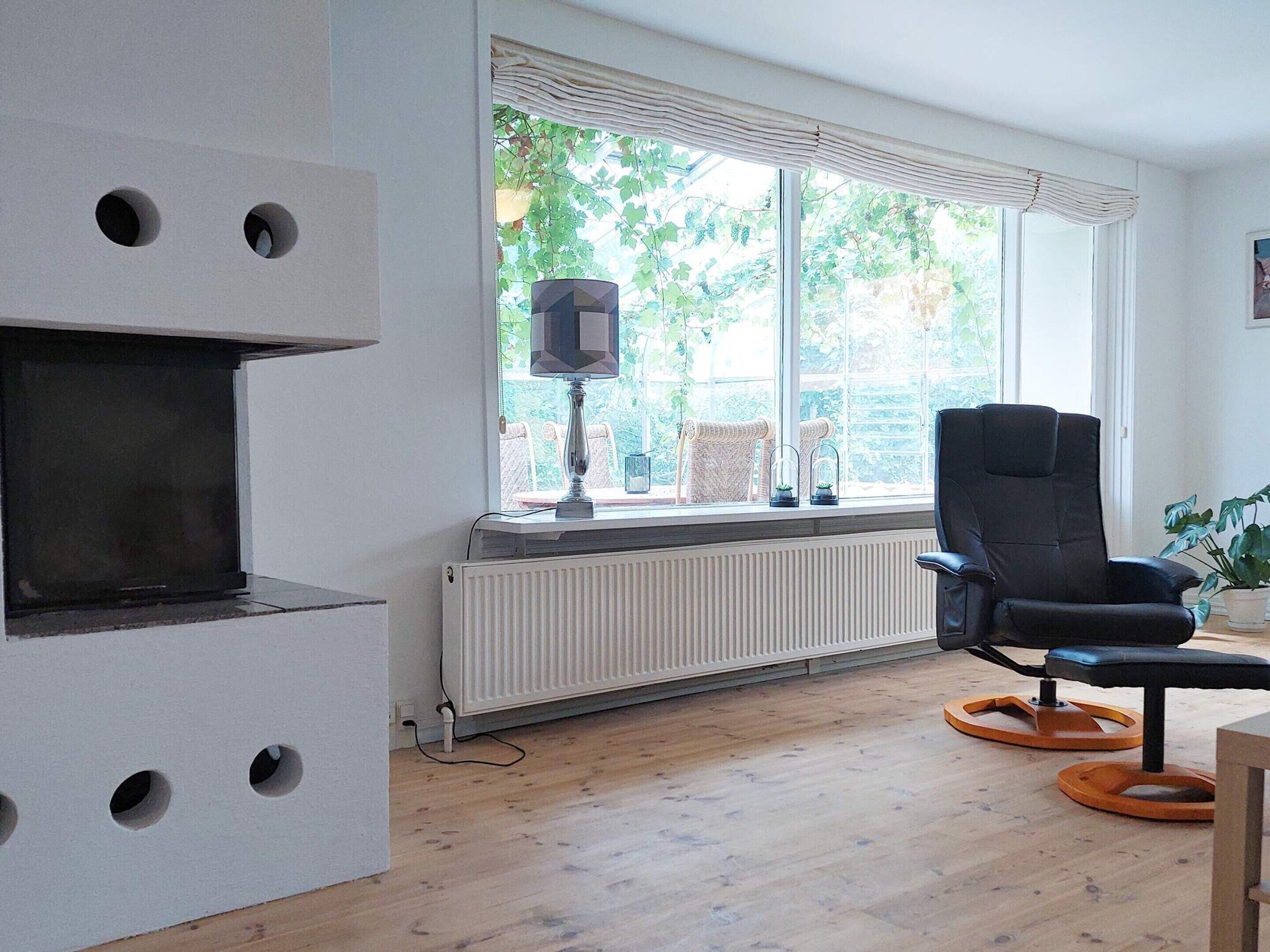 A room with a fireplace, a large window with blinds, a black chair, and a radiator.