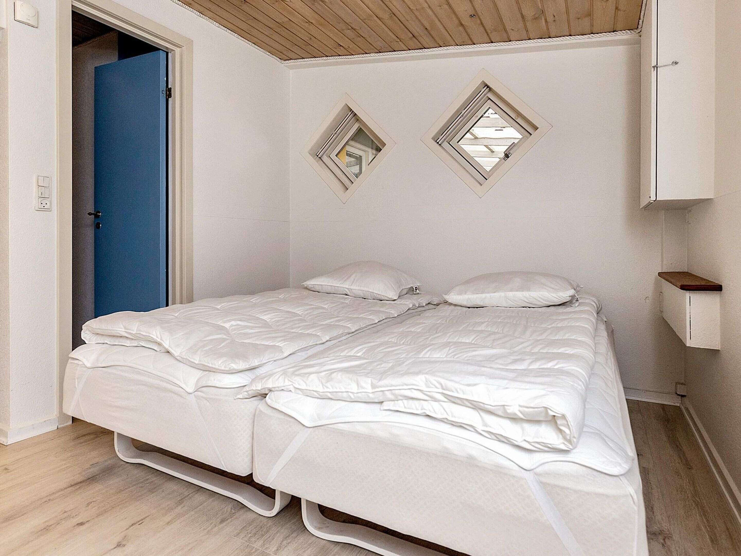 A single-bed room with a wooden ceiling, a blue door, and a white wall with two diamond-shaped mirrors.