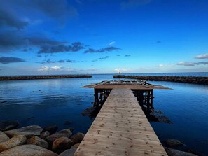 A wooden pier extending into calm waters, leading to a rocky breakwater with a lighthouse in the distance. - 6 Person Holiday Home in Albaek (Aalbaek)