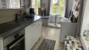 Kompakti keittiö, jossa on pesuallas, liesi sekä ruokailutila, jossa on pöytä ja penkki.