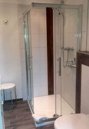 A modern bathroom with a glass-enclosed shower, a white toilet, and a wooden floor.