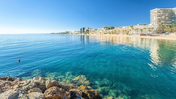 A coastal view with clear blue waters, a rocky shoreline, and a beachfront hotel with multiple floors and balconies. - Villa in Spain Near Stunning Beaches (Roquetas de Mar)