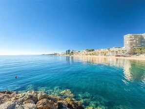 A coastal view with clear blue waters, a rocky shoreline, and a beachfront hotel with multiple floors and balconies. - Villa in Spain Near Stunning Beaches (Roquetas de Mar)