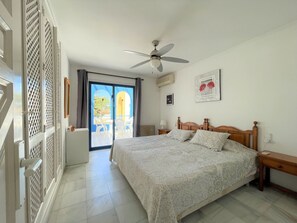 A bedroom with a bed, a ceiling fan, a window with a view of the outside, and a door with a louvered design.