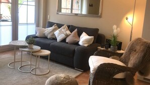 A living room with a dark-colored sofa, a round side table, a wicker chair, and a floor lamp. - Holiday Vacation by the sea (Scharbeutz)
