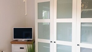 A room with a television on a wooden surface, a white cabinet with drawers, and a large white door with frosted glass panels. - Holiday Vacation by the sea (Scharbeutz)