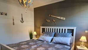 A bedroom with a bed, two bedside tables, a wall-mounted lamp, and a decorative fish-shaped object. - Holiday Vacation by the sea (Scharbeutz)