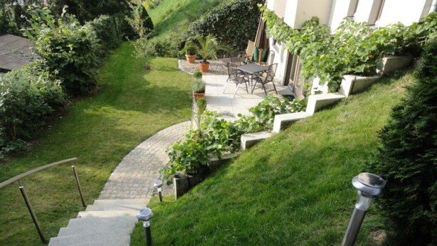 Eine Steintreppe führt zu einer Terrasse mit Gartenmöbeln und Topfpflanzen.
