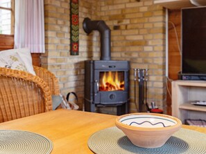 A cozy living room with a brick wall, a fireplace, a television, and a wicker chair. - 6 Person Holiday Home in Vaeggerlose (Vaeggerlose)