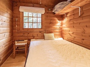 A wooden cabin room with a bed, a small chair, a window, and a wall-mounted shelf. - 6 Person Holiday Home in Vaeggerlose (Vaeggerlose)