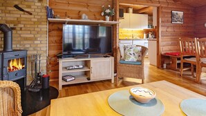 A cozy cabin interior with a wood-burning stove, a television, wicker furniture, and a kitchen area. - 6 Person Holiday Home in Vaeggerlose (Vaeggerlose)