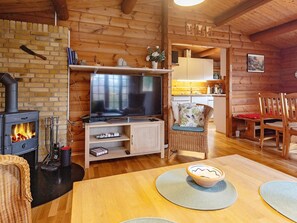 A cozy cabin interior with a wood-burning stove, a television, wicker furniture, and a kitchen area. - 6 Person Holiday Home in Vaeggerlose (Vaeggerlose)