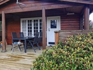 A wooden cabin with a covered porch, a dining table with chairs, and a small garden area. - 6 Person Holiday Home in Vaeggerlose (Vaeggerlose)