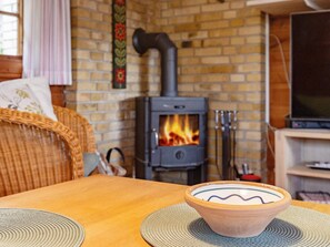 A cozy room with a brick wall, a wood-burning stove, a television, and a wicker chair. - 6 Person Holiday Home in Vaeggerlose (Vaeggerlose)
