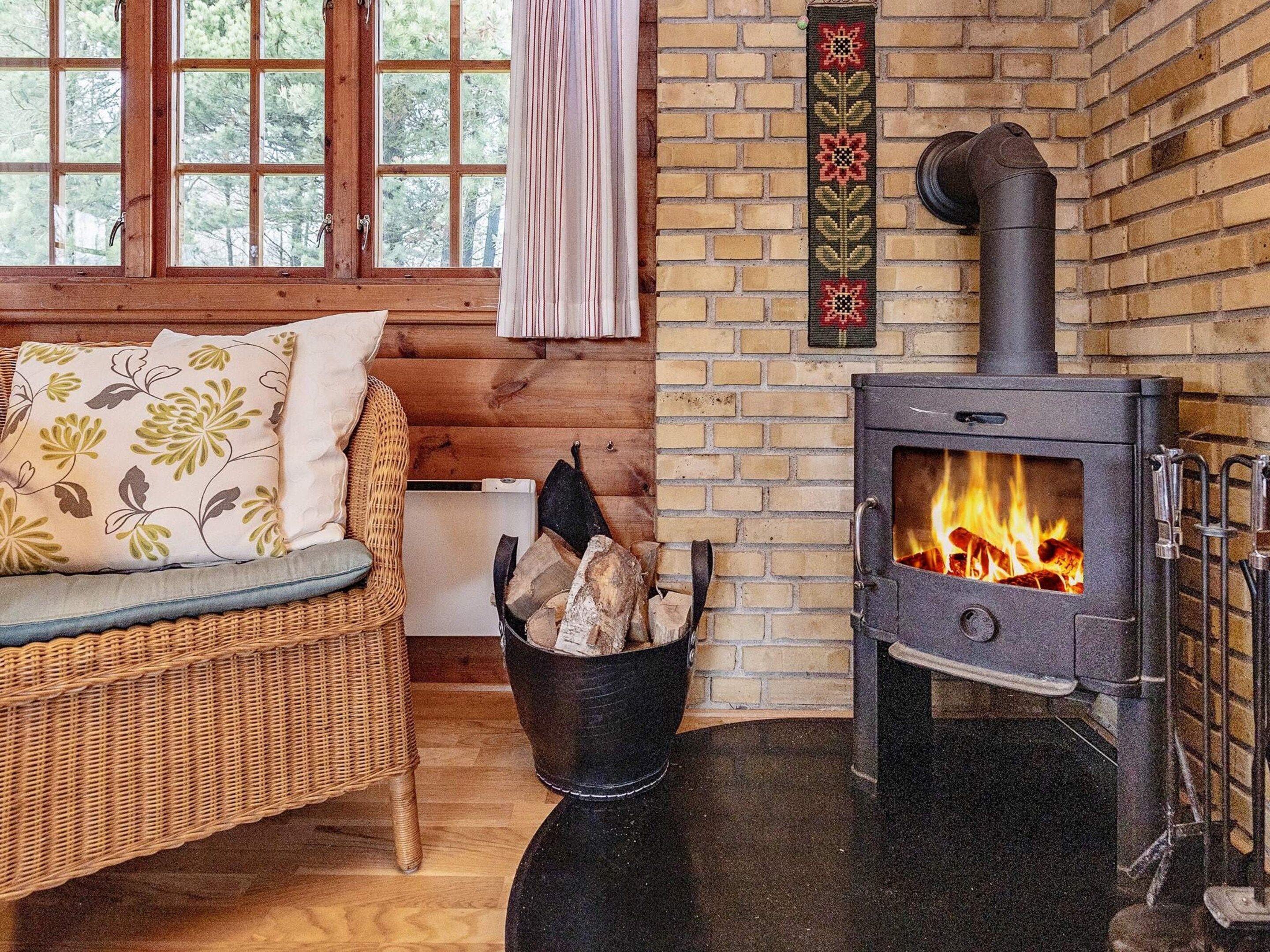 A cozy room with a wicker sofa, a fireplace with logs, and a brick wall.