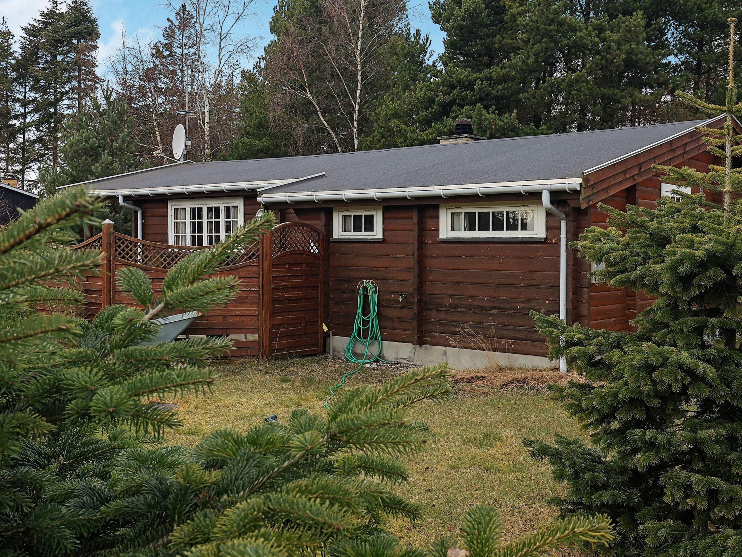 A cabin with a wooden exterior, a covered porch, and a green hose.