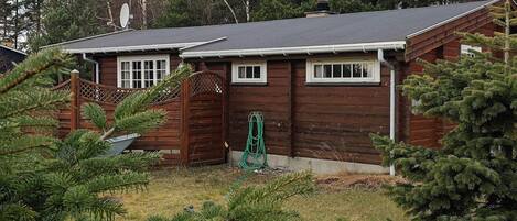 A cabin with a wooden exterior, a covered porch, and a green hose.