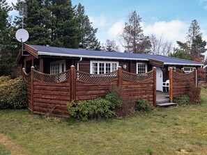 A wooden cabin with a fenced porch, satellite dish, and a small outdoor seating area. - 6 Person Holiday Home in Vaeggerlose (Vaeggerlose)