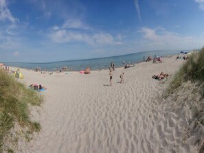 Une plage de sable où des gens se prélassent au soleil et se baignent.