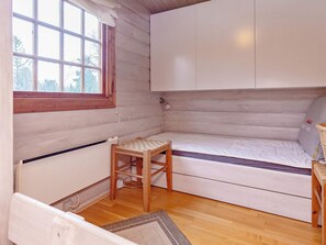 Une petite pièce agréable et chaleureuse, avec un plancher en bois, un lit simple, une petite table et une fenêtre donnant sur les arbres.