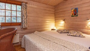 A cozy cabin room with a bed, a wicker chair, a window with curtains, and a painting on the wall. - 6 Person Holiday Home in Vaeggerlose (Vaeggerlose)