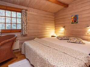 A cozy cabin room with a bed, a wicker chair, a window with curtains, and a painting on the wall. - 6 Person Holiday Home in Vaeggerlose (Vaeggerlose)
