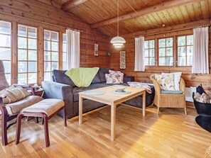 Un interior acogedor de cabaña con sofá, sillón, mesa y chimenea.