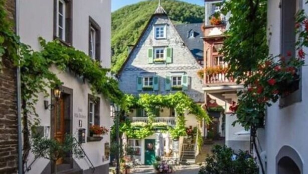 Une rue pavée menant à un bâtiment traditionnel doté d’un toit en pente et de volets verts.