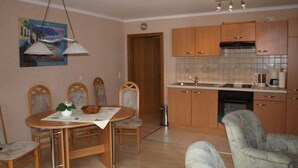 Une cuisine compacte avec des meubles de rangement en bois, une table à manger avec des chaises et un fauteuil à motifs.