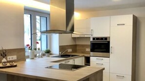 A modern kitchen with a central island, bar stools, a built-in oven, and white cabinetry. - Spacious Apartment Near Ski-lift (Neuhütten)