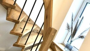 A wooden spiral staircase with a view of pampas grass through a window. - Spacious Apartment Near Ski-lift (Neuhütten)