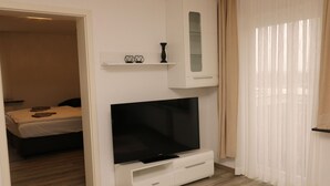 Une chambre d’hôtel avec un lit, un téléviseur posé sur un meuble, une petite armoire et une fenêtre avec des rideaux.