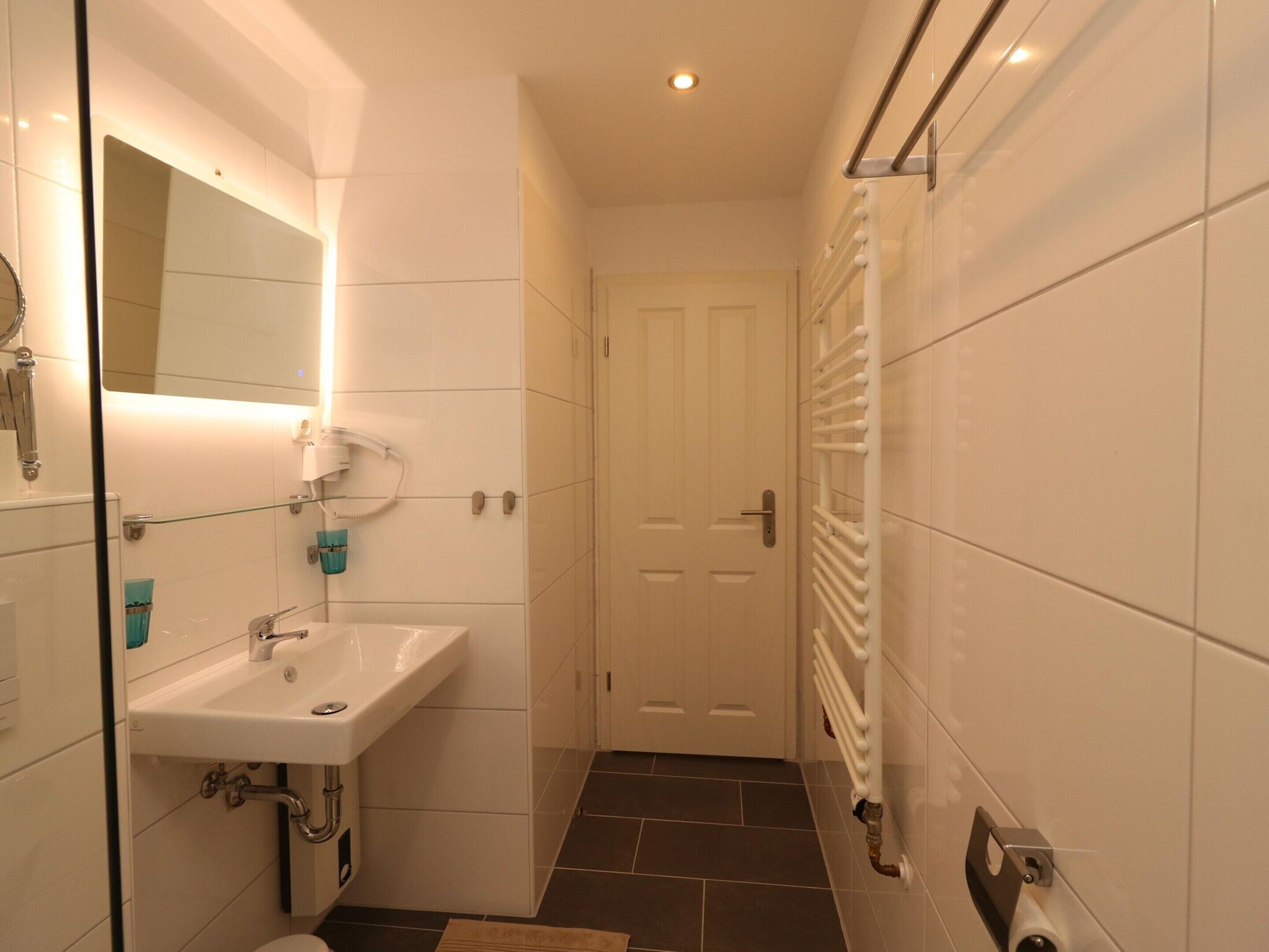 A narrow bathroom with a white sink, a mirror, and a towel rack.