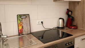 Une cuisine moderne dotée d’une plaque de cuisson à induction noire, d’un évier en acier inoxydable, d’une machine à café rouge et d’une planche à découper en bois ornée de motifs de fruits.