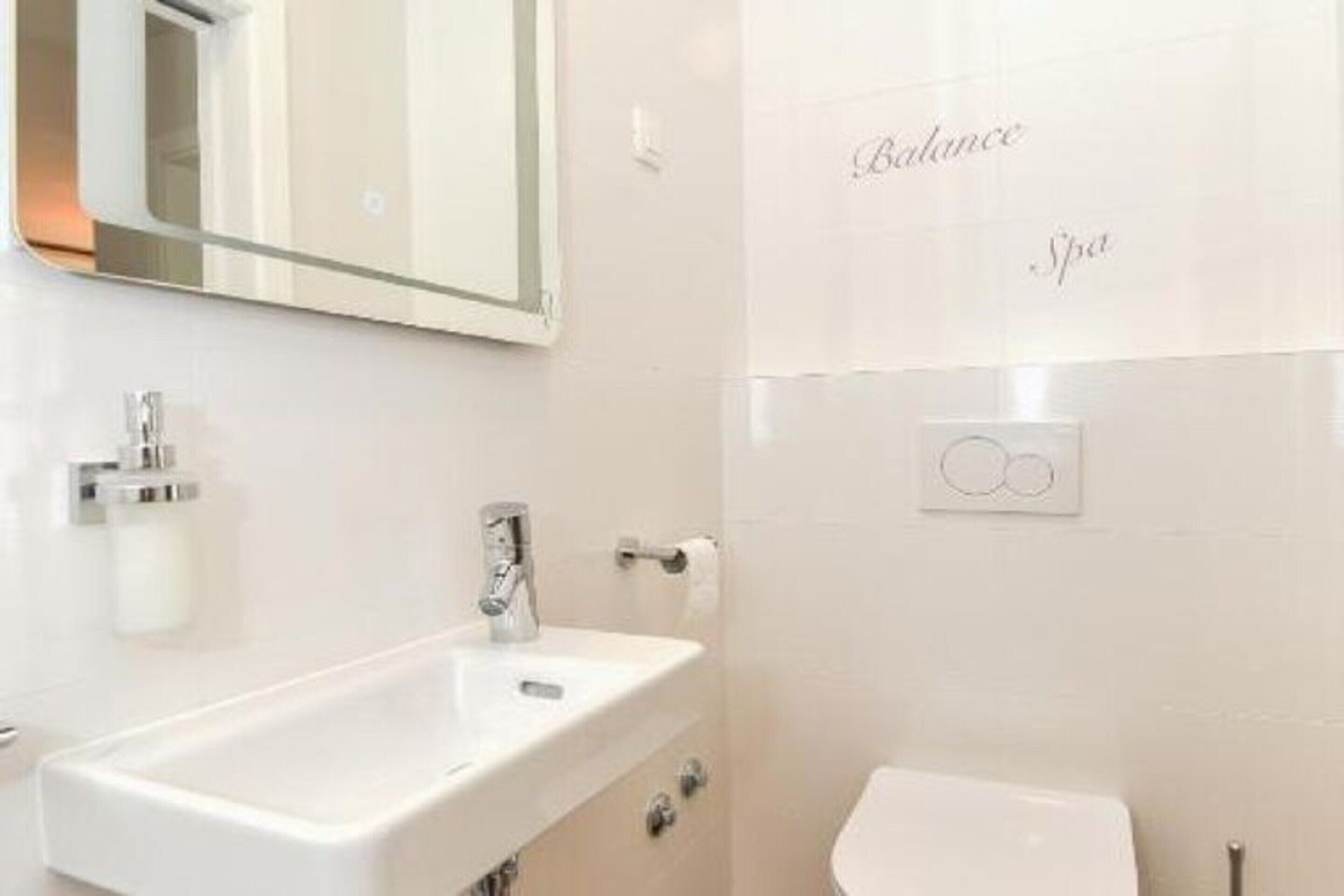 A modern bathroom with a white sink, mirror, and toilet. The wall has a spa-themed design with the words "Balance Spa" visible.