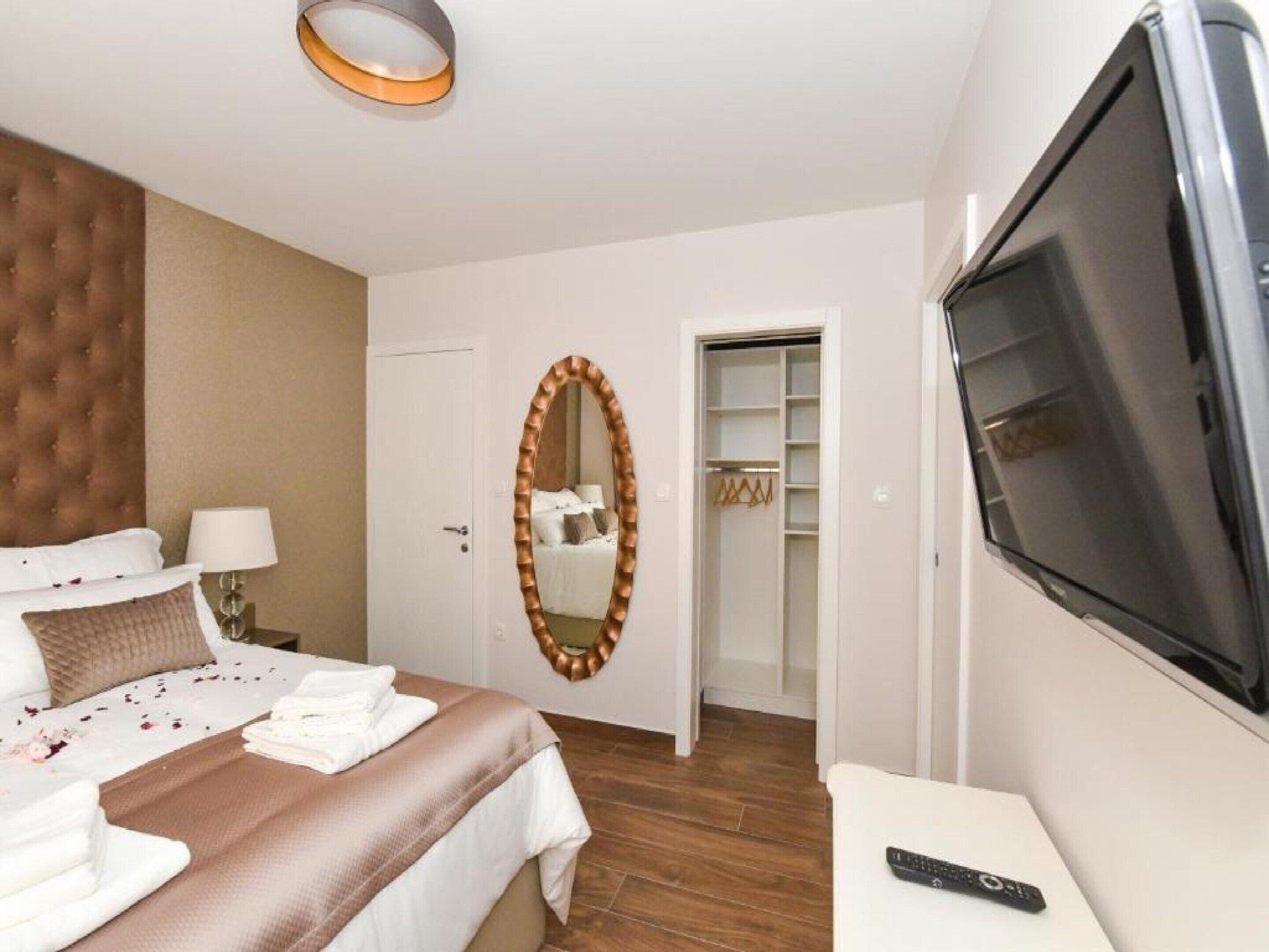 A hotel room with a bed, a TV, a mirror, a wardrobe, and a bedside table.