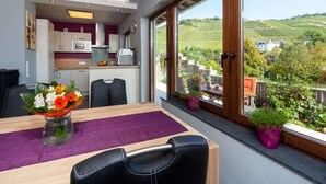 A modern kitchen with a view of vineyards, a dining area with a purple tablecloth, and a large window with a view of the countryside. - Holiday Home Moselle Valley (Maring-Noviand)