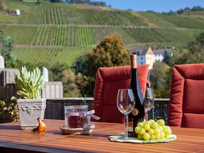A table set outdoors with a bottle of wine, two wine glasses, a bunch of grapes, a small jar with a candle, and a rooster figurine. - Holiday Home Moselle Valley (Maring-Noviand)