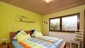A bedroom with two beds, a wooden ceiling, a window with a view, and a wall with a decorative sign. - Holiday Home Moselle Valley (Maring-Noviand)