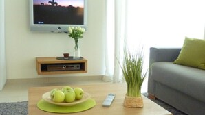 A living room with a television on a stand, a small table with apples and a remote control, and a grey sofa with a green pillow. - Deck 4 Modern Retreat (Timmendorfer Strand)