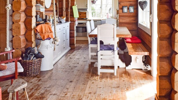 A rustic cabin interior with a wooden floor, a dining table, a kitchen area with a stove, and a large window providing natural light. - 6 Person Holiday Home in Hurdal (Hurdal)