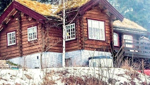 A wooden cabin with a thatched roof, surrounded by trees and snow. - 6 Person Holiday Home in Hurdal (Hurdal)