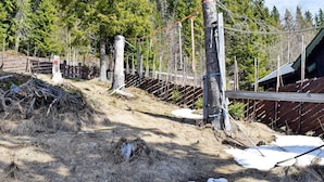 A fenced outdoor area with a wooden structure, possibly a cabin or storage shed, surrounded by trees and snow patches. - 6 Person Holiday Home in Hurdal (Hurdal)
