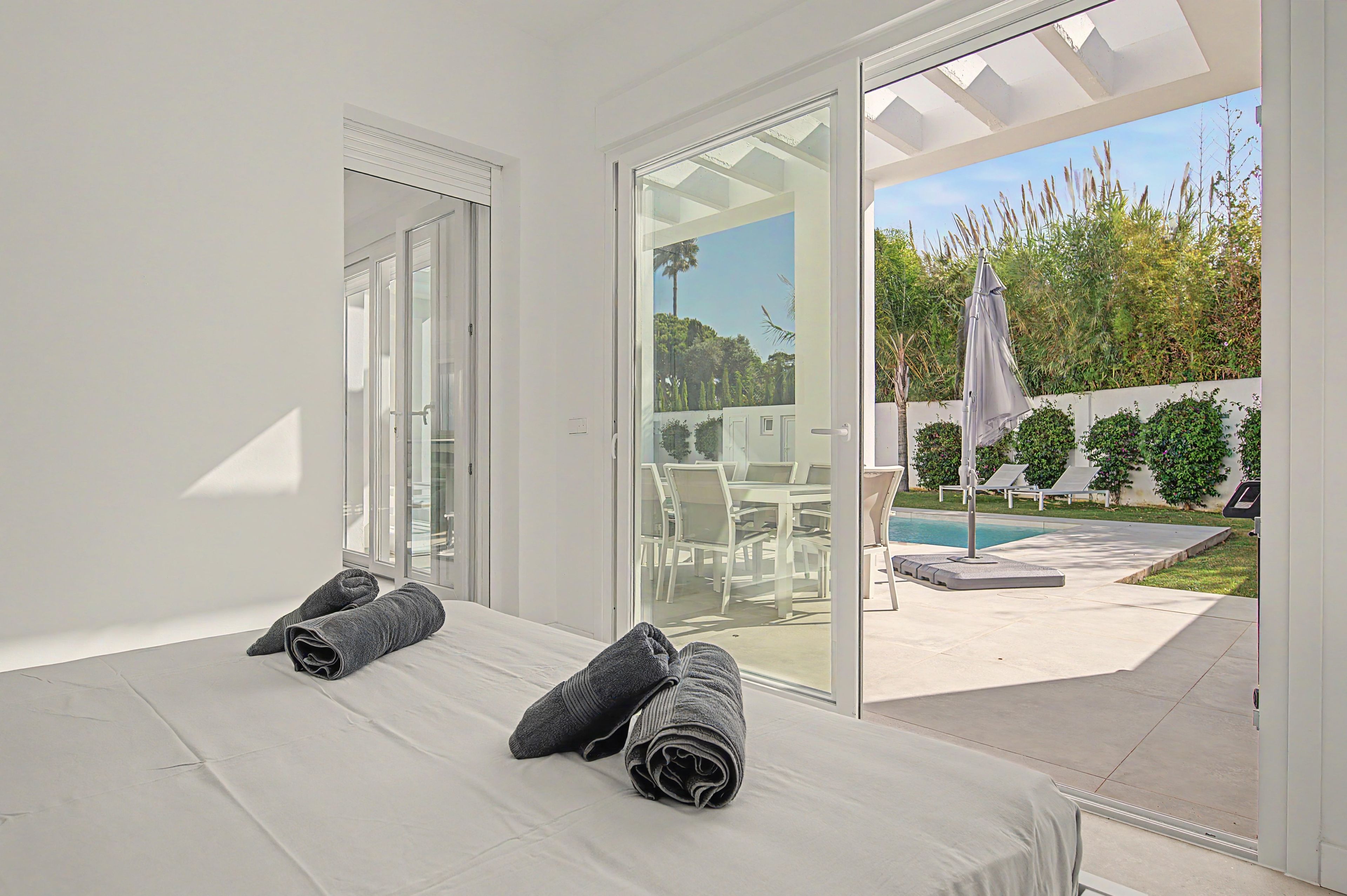 Un dormitori amb un llit, una porta de vidre que dona a un pati amb piscina i mobles d'exterior.