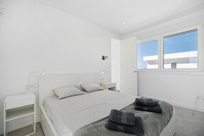 Et moderne soveværelse med seng, sengeborde, et natbord, et vindue med udsigt og en dør.